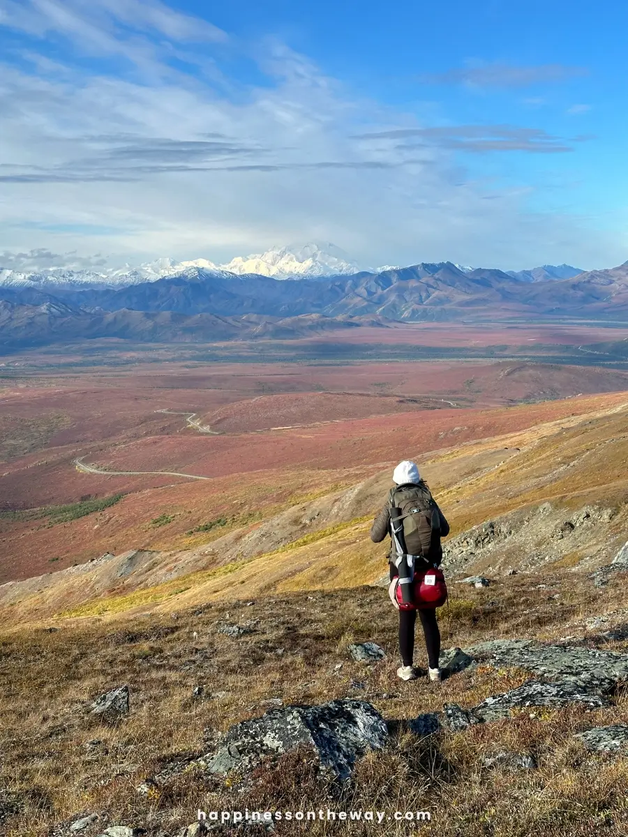 Me standing on a rocky hillside in a remote wilderness, wearing a backpack and carrying camping gear.