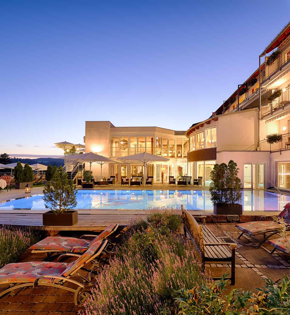 Hotel Kronelamm at twilight with a well-lit modern exterior, large glass windows, and an inviting outdoor pool reflecting the warm lights.