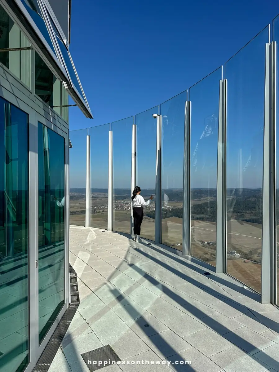 A wider perspective of the glass observation deck, with me standing near the edge, looking at the landscape.