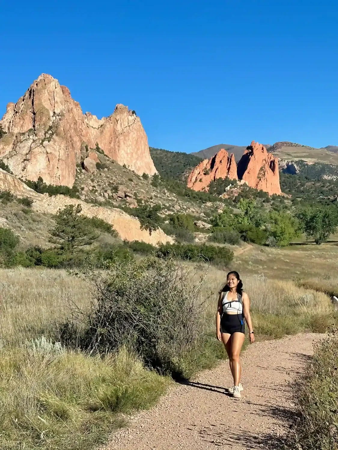 Woman hiking on a sunny day in Garden of the Gods, Colorado, surrounded by red rock formations and blue skies.