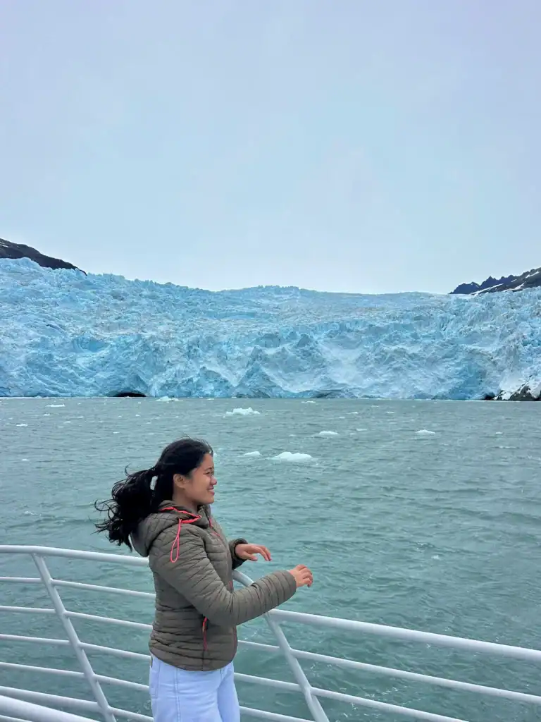 Smiling woman on a boat with a glacier in the background during a volunteer trip in Alaska