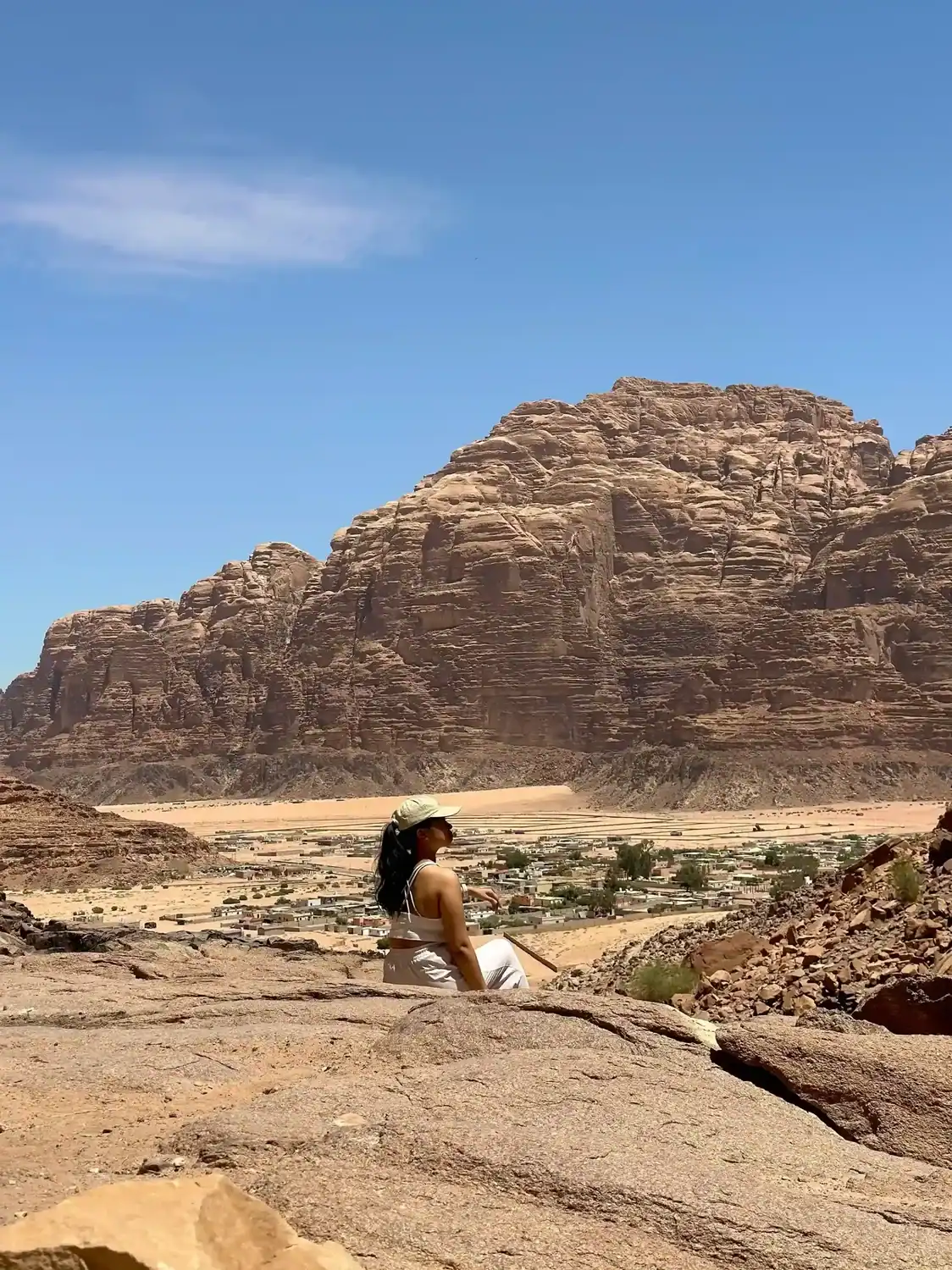 A person sits atop a rocky hill overlooking Wadi Rum Village in Jordan, surrounded by desert landscape and golden light. The quiet moment captures the essence of slow travel vs fast travel