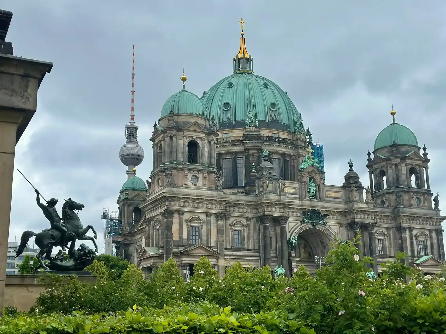 Berlin Cathedral with its striking green dome and ornate architecture stands prominently against a cloudy sky.