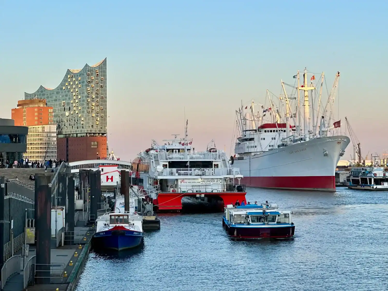 Hamburg harbor at sunset, showcasing the modern Elbphilharmonie concert hall with its wavy glass façade.