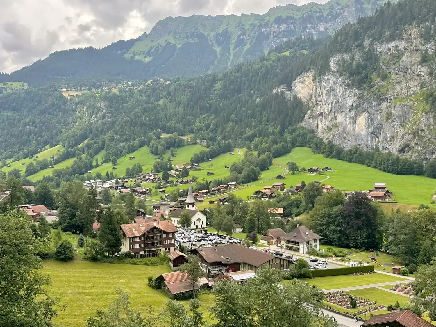 Charming alpine village of Lauterbrunnen nestled in a lush green valley, surrounded by steep cliffs and forested mountains.