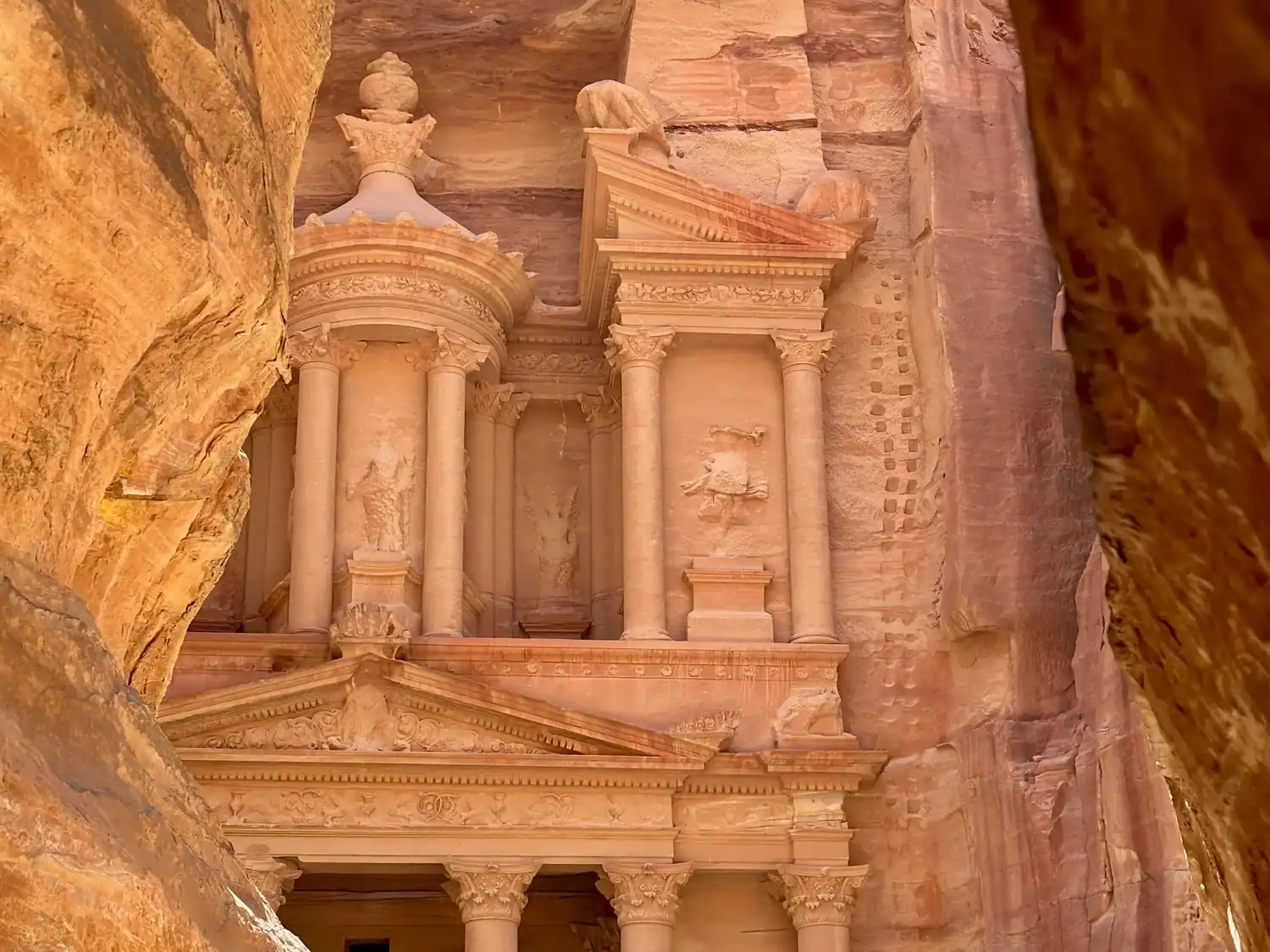 The iconic façade of Al-Khazneh, or "The Treasury," in Petra, Jordan, carved into rose-colored sandstone cliffs.