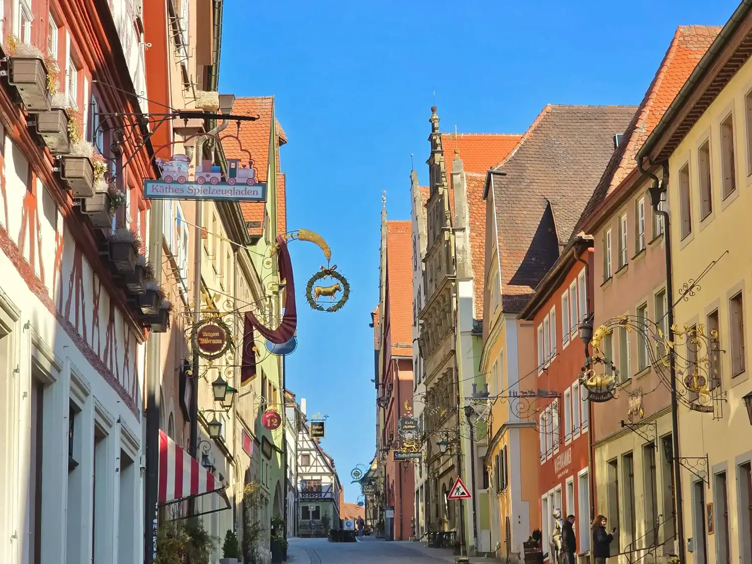 Charming medieval street in Rothenburg ob der Tauber lined with colorful half-timbered buildings and wrought-iron shop signs.