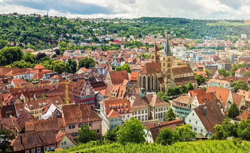 Panoramic view of Stuttgart, Germany, featuring red-roofed houses, lush greenery, and the prominent Stiftskirche (Collegiate Church) at the center.