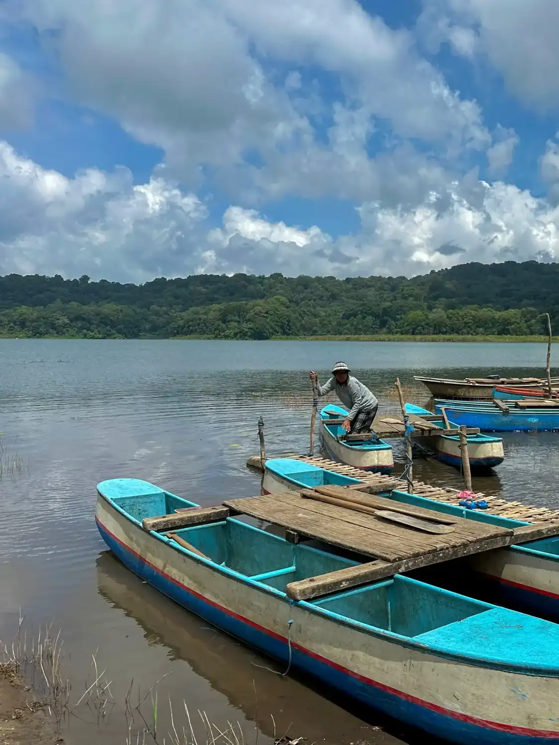 A man stands beside traditional wooden boats on the edge of Lake Tamblingan in Munduk, Bali.