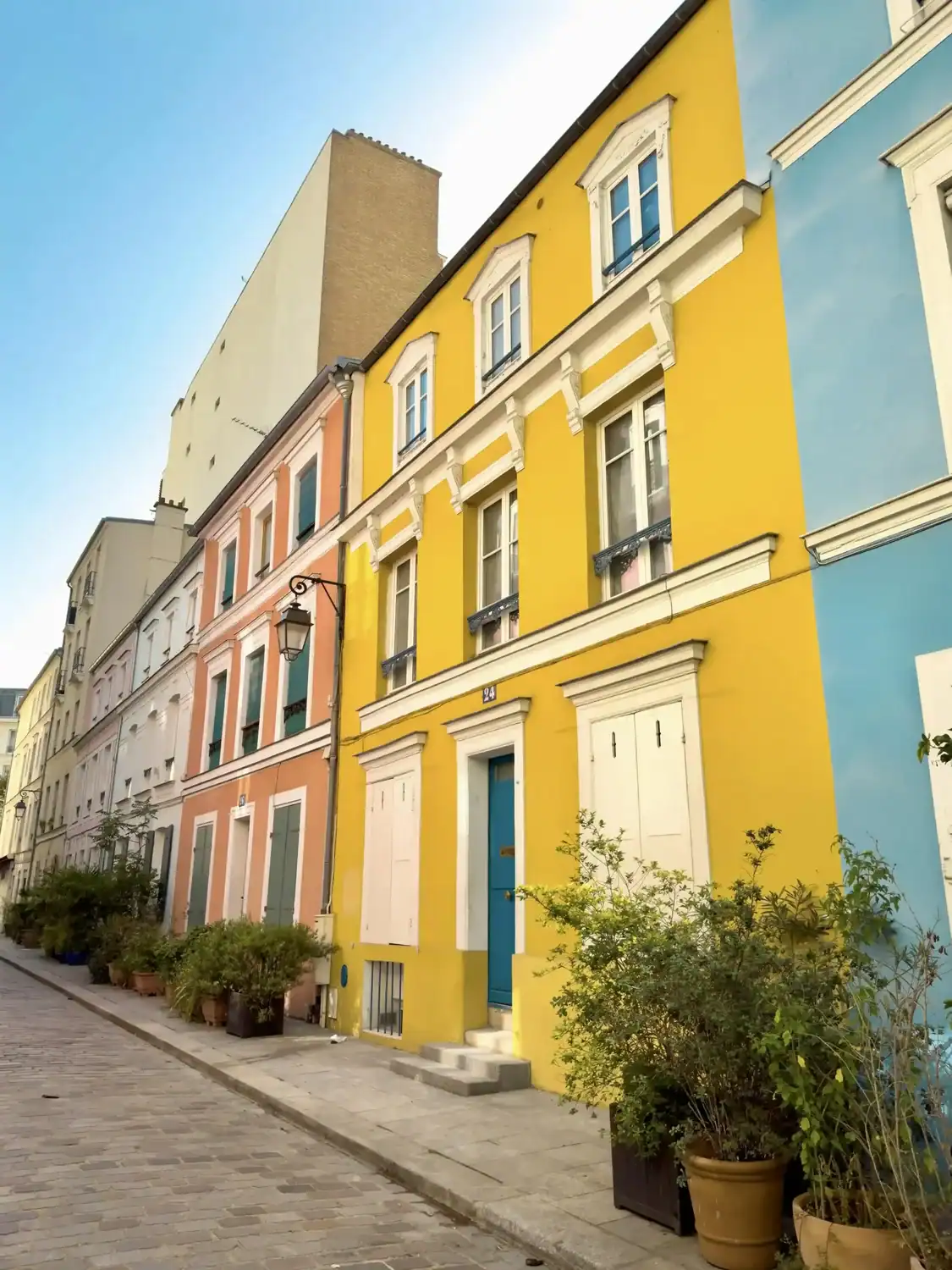 Colorful pastel townhouses line the cobblestone street of Rue Crémieux in Paris, with vibrant facades in yellow, blue, and pink. 