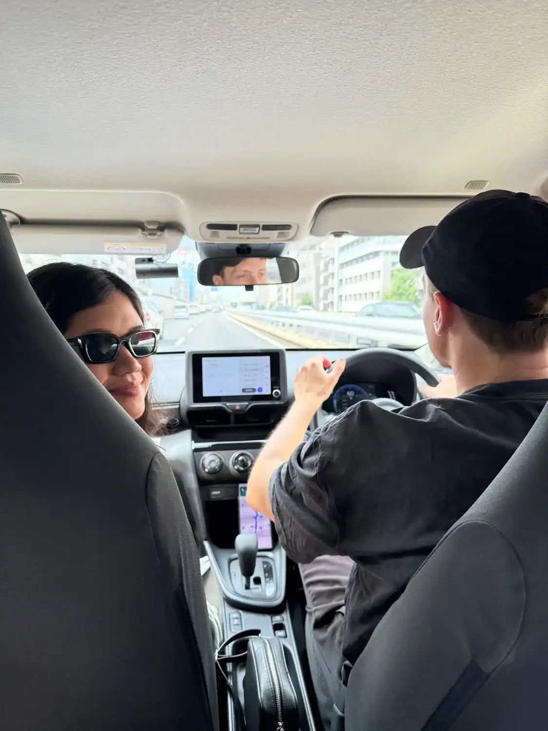 Inside the car during a road trip in Japan, with GPS navigation on screen and a view of city streets ahead.
