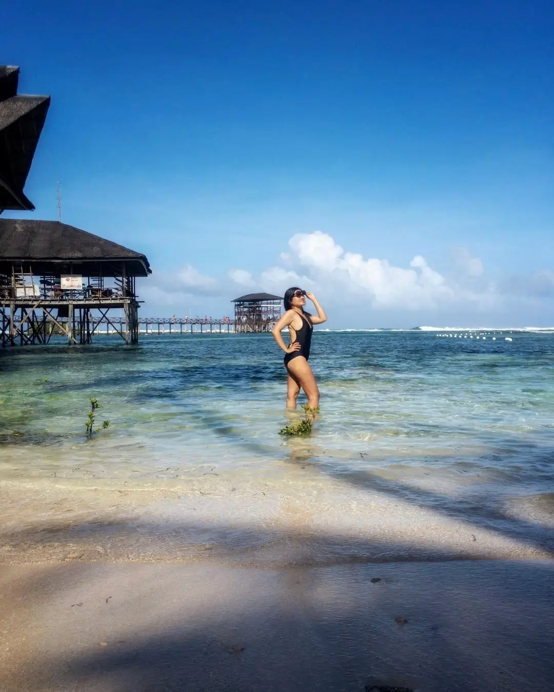 A woman standing in shallow water at Cloud 9 Beach in Siargao, with the wooden boardwalk and viewing tower in the background under a clear blue sky. Exploring best beaches in Siargao