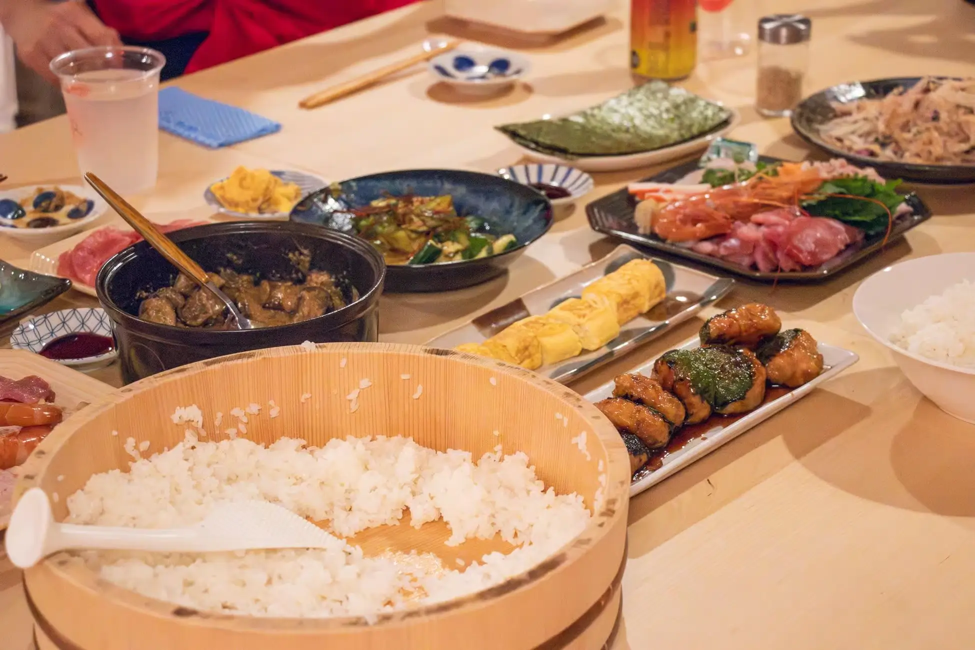 A table set with various Japanese dishes including sushi rice, tamagoyaki, grilled skewers, sashimi, and side dishes during an izakaya-style cooking class in Tokyo.
