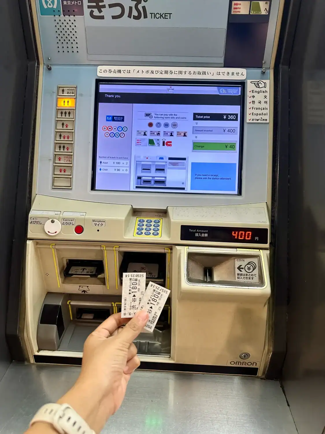 Hand holding Tokyo Metro single-ride tickets in front of a ticket machine showing ¥360 fare