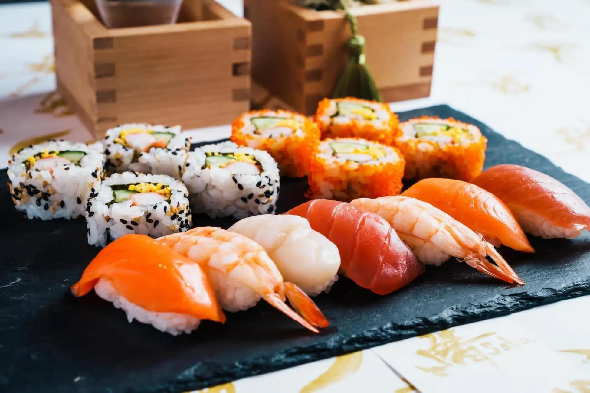 A plate of assorted sushi including salmon, shrimp, tuna, scallop nigiri, and colorful sushi rolls arranged neatly on a slate board.