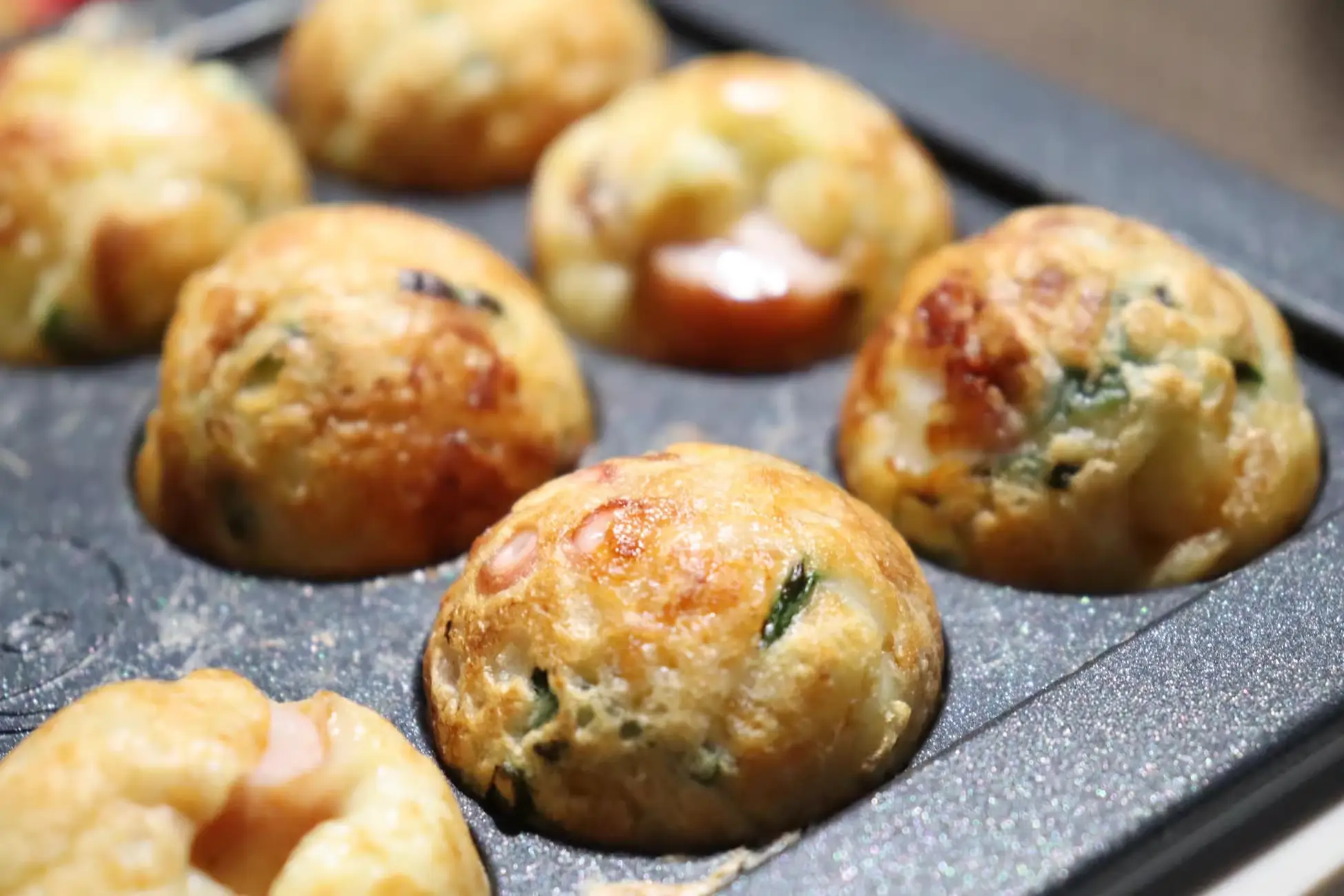 Takoyaki cooking on a hot griddle, showing golden, round batter balls with bits of seafood and green onion.