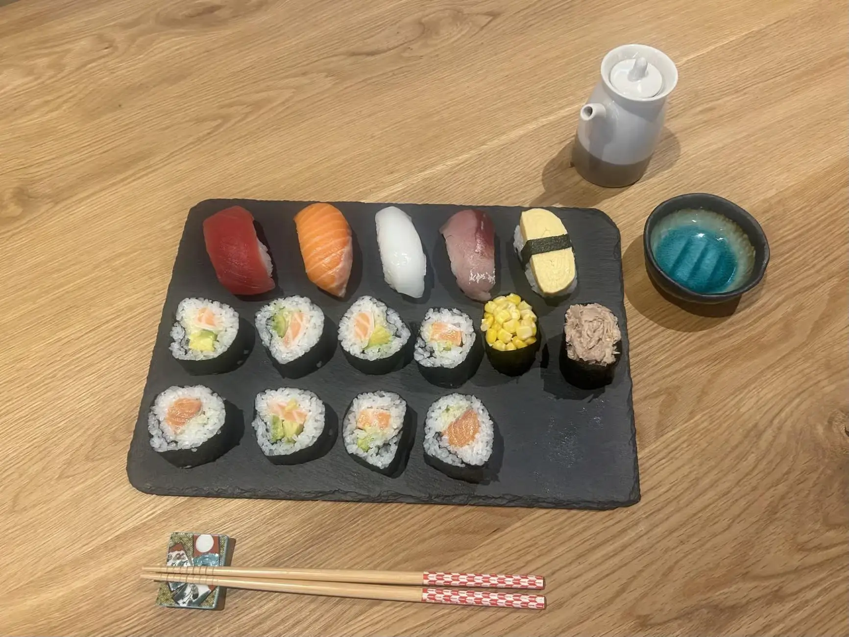 Assorted homemade sushi rolls and nigiri displayed on a black slate board