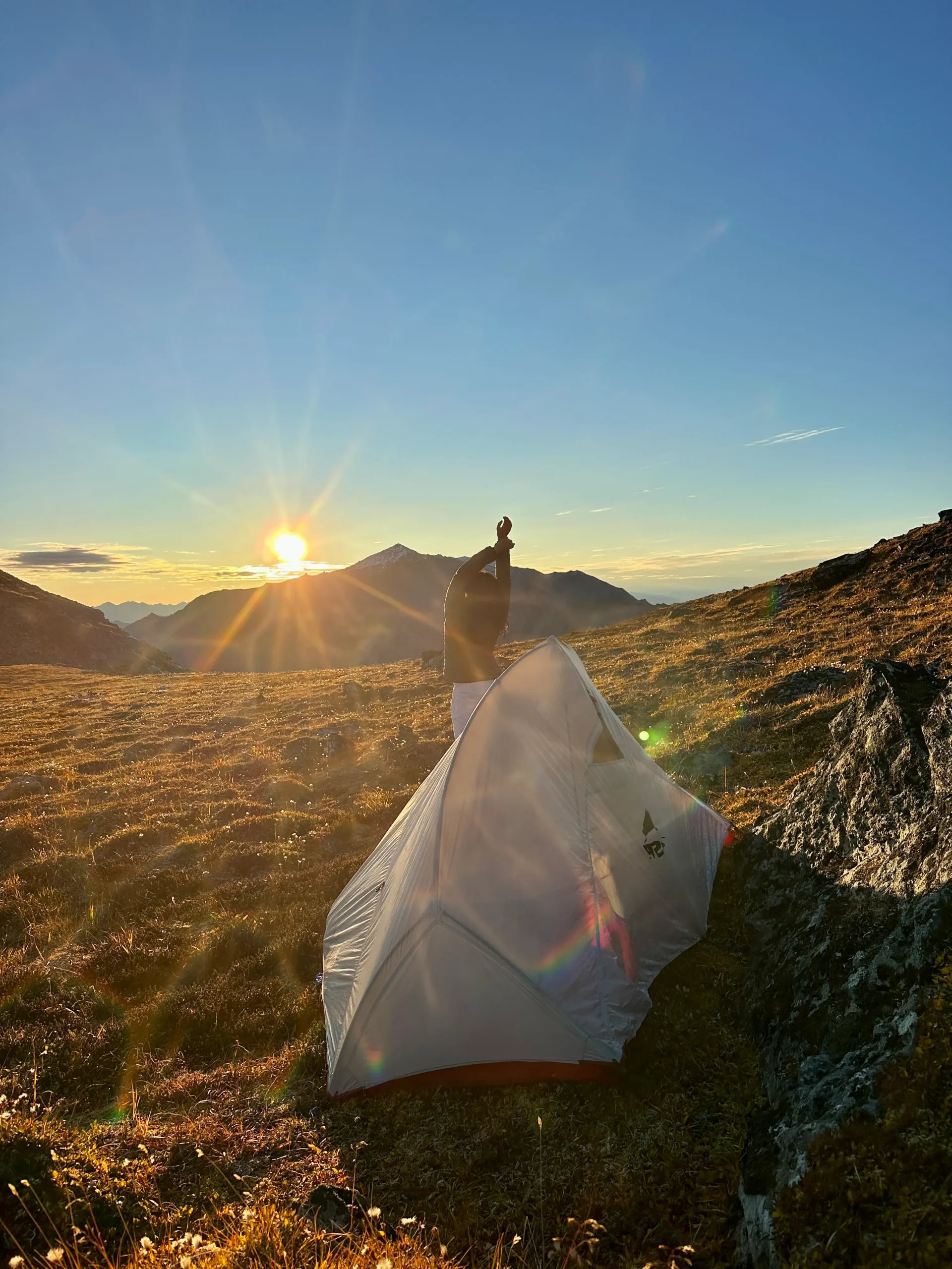 Travel blogger camping in Denali National Park doing yoga at sunrise beside a tent with mountain peaks in the background.