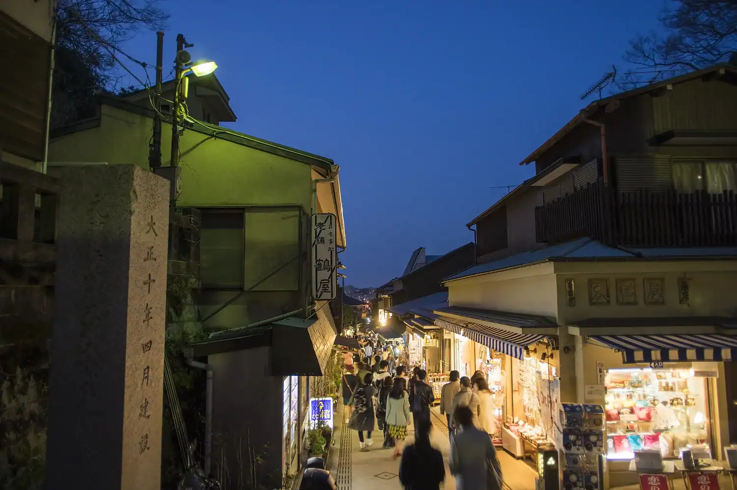 Enoshima's Nakamise shopping street at dusk with illuminated storefronts and visitors walking through narrow alley