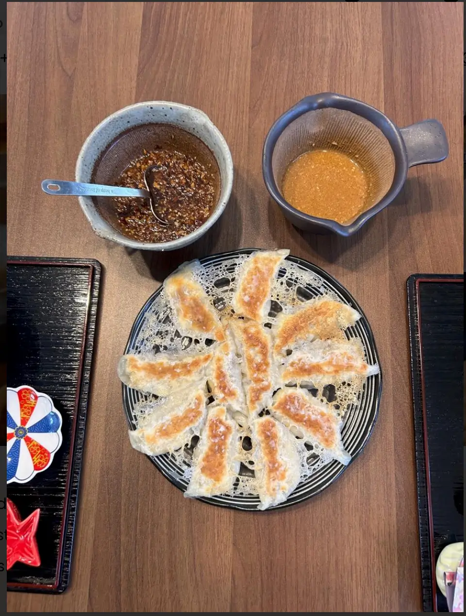 Japanese gyoza arranged in a circular pattern with crispy lace edges, served with two dipping sauces in ceramic bowls, one dark soy-based and one creamy sesame-based.