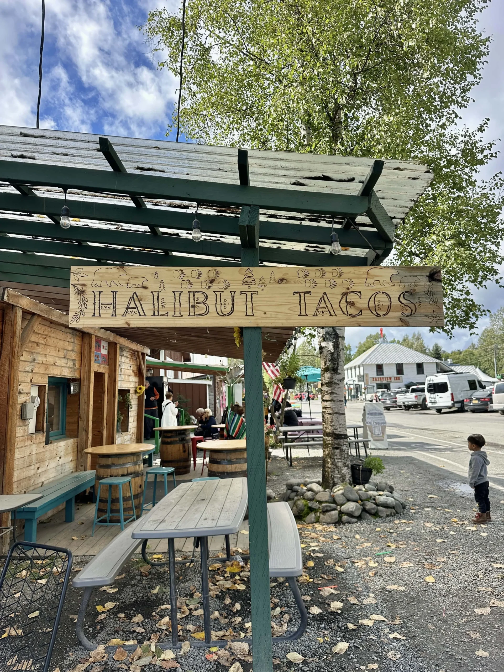 A sign hanging from a green roof that says "Halibut Tacos," the most famous meal in Talkeena Tako, one of the best places to eat in Talkeena.