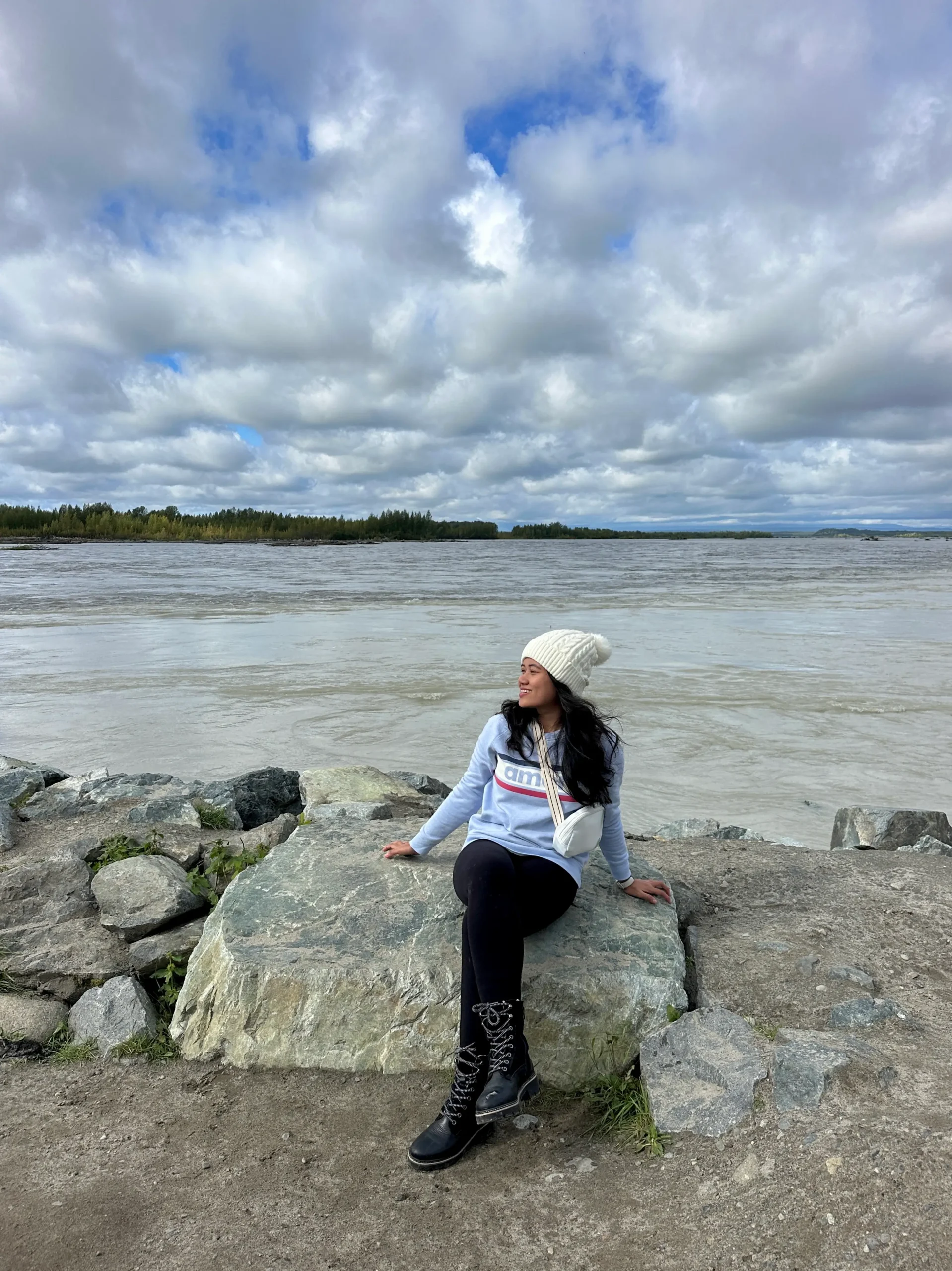 Gladis sitting on large rocks along the water’s edge while hiking the Talkeetna Lakes Trail.