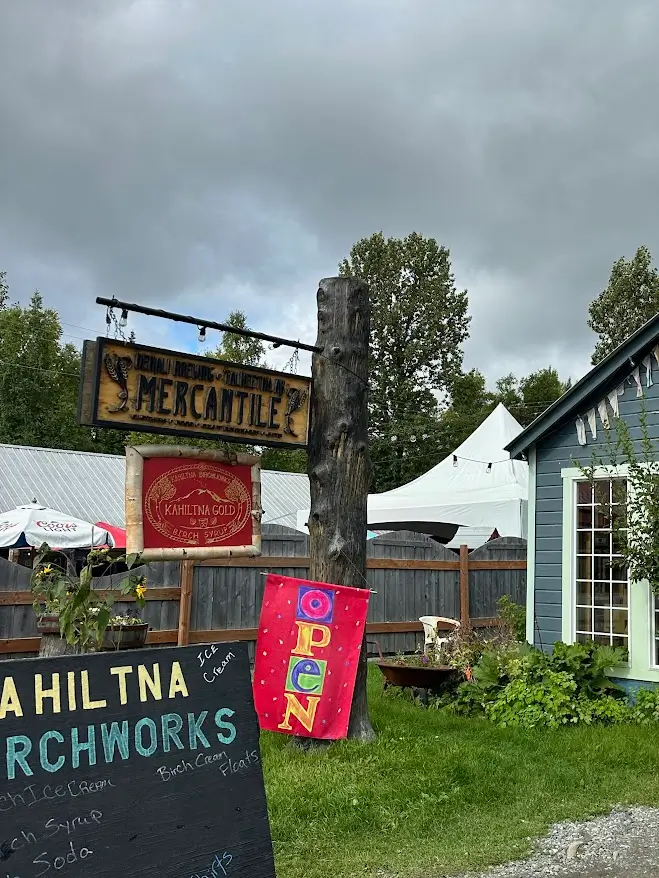 Wooden signs that read "Kahiltna Birchworks" and a snippet of a blue cabin in Talkeetna, Alaska.