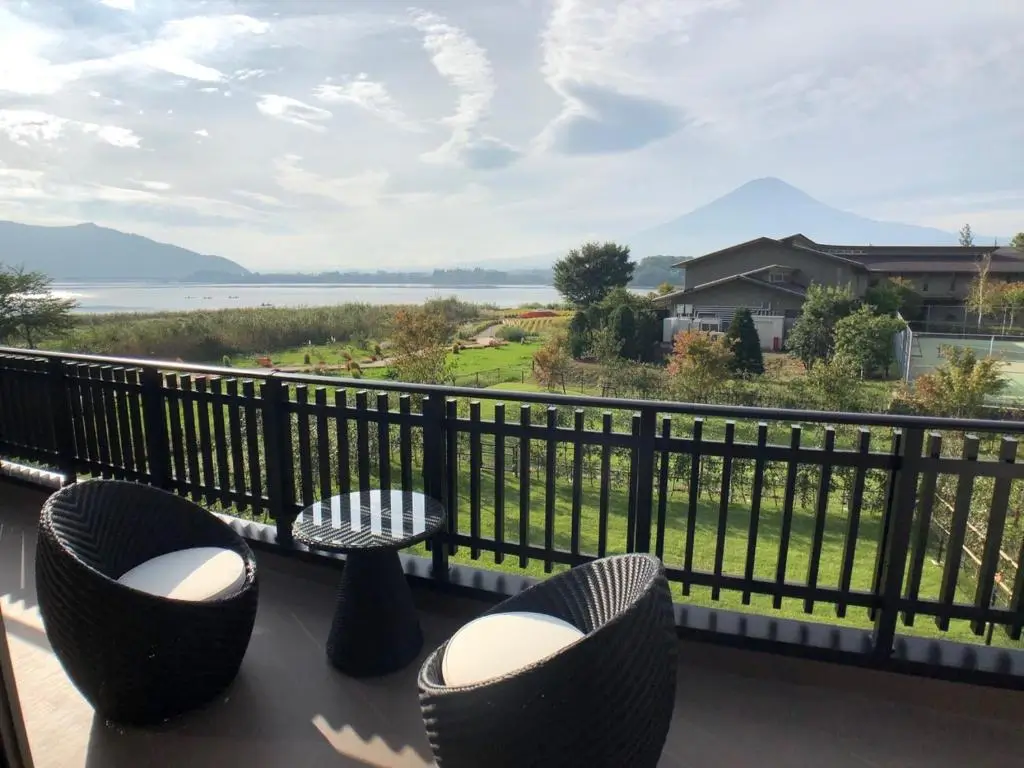 Serene lakeside view from a balcony with modern outdoor furniture, overlooking lush greenery and distant mountains, perfect for happiness.