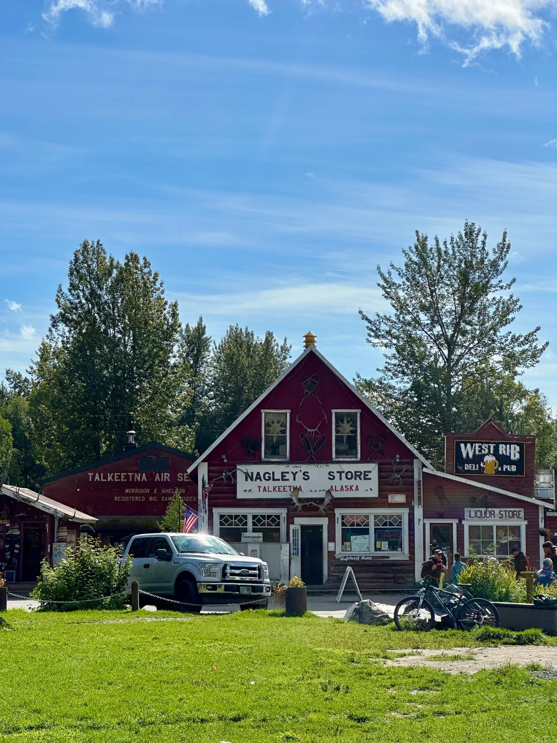 Front view of Nagley’s Store, a red barn-like building surrounded by grass and trees, with a white car parked nearby.
