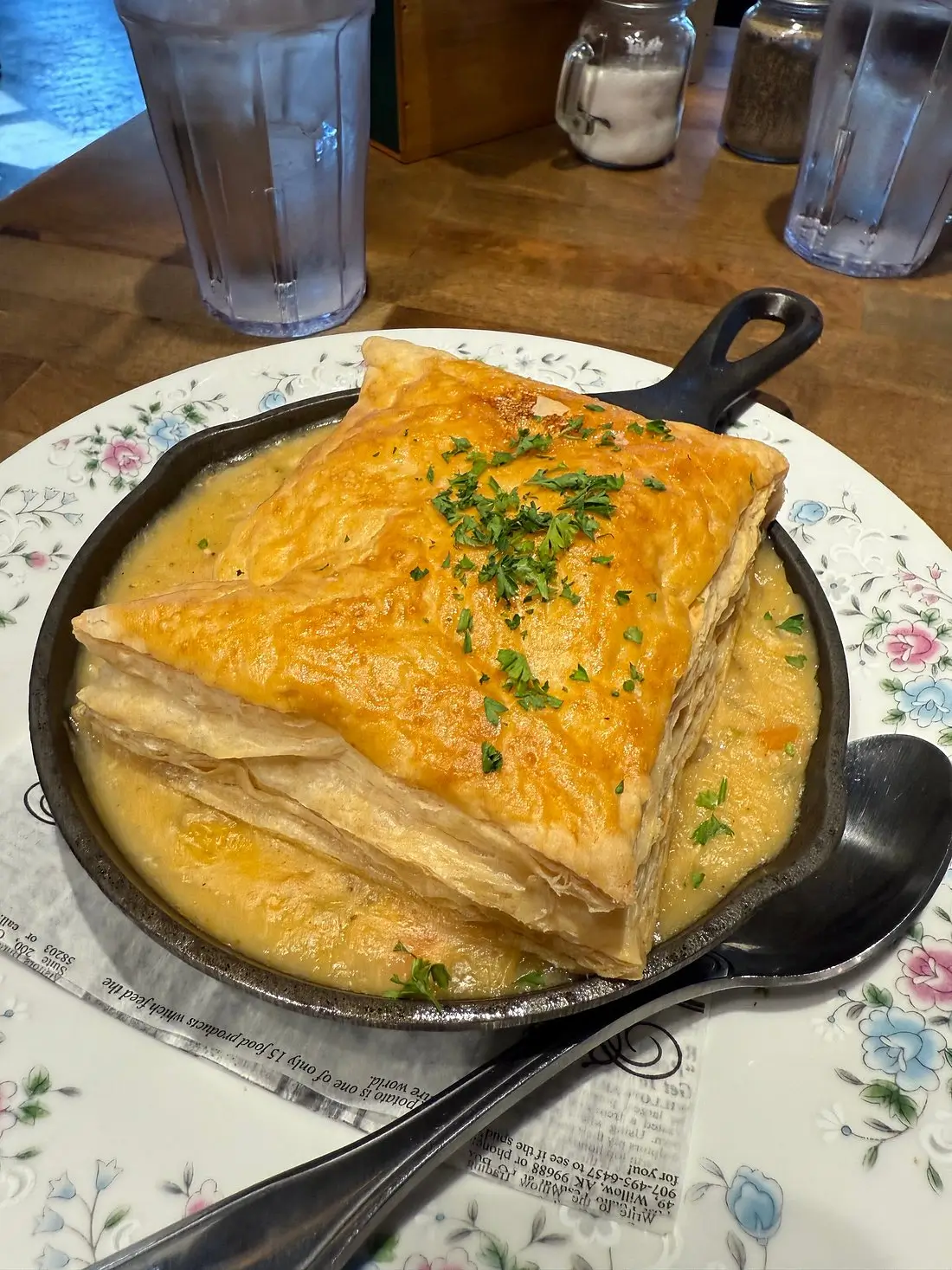 On a white table in Homestead Kitchen sits a large black pan almost overflowing with golden layers of puff pastry, dough, and seafood.