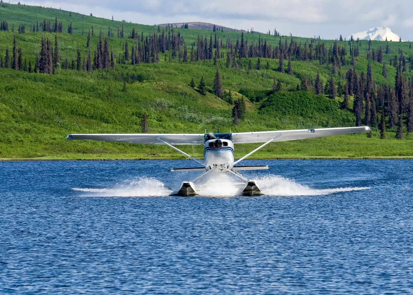 A seaplane taking off from a lake surrounded by green hills in Talkeetna, Alaska.