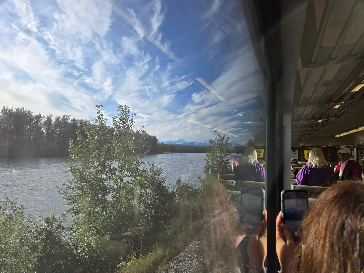 Views of a river, trees, and mountains reflected in the Hurricane Turn Train window.