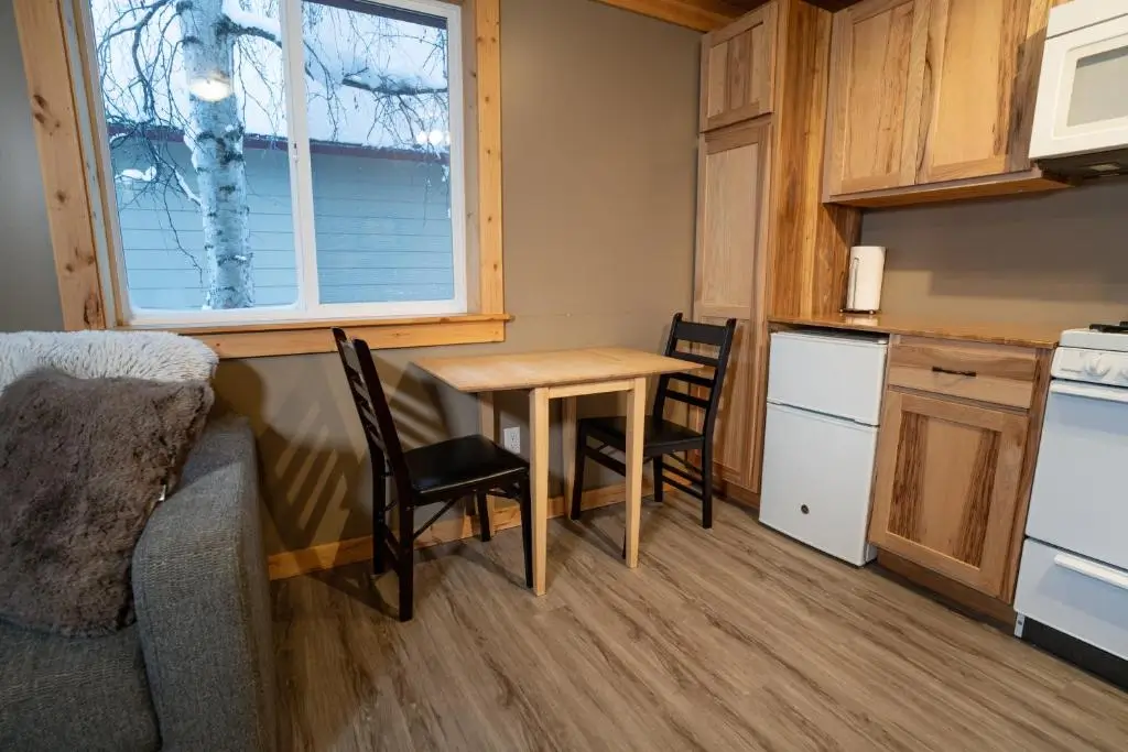 The living space of The Talkeetna Landing, featuring a wooden table with two black chairs, a stove, and wooden cabinets.