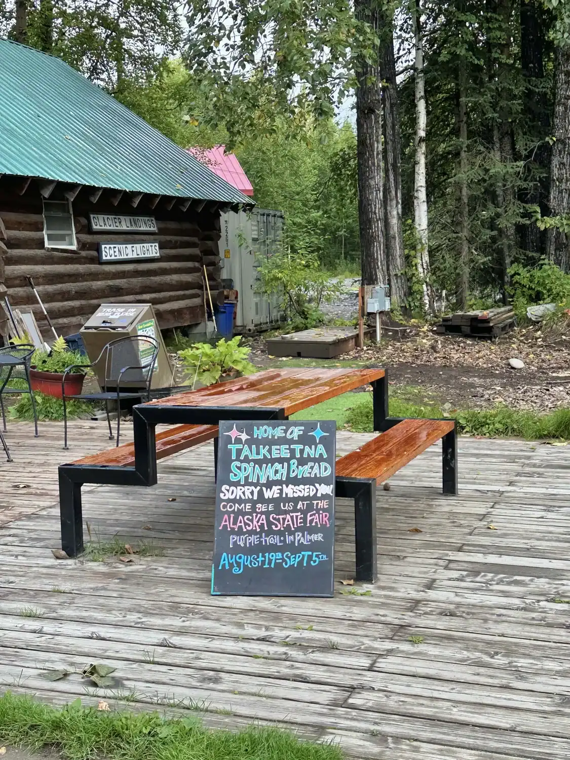 A sign leaning on a wooden bench with the words, "Talkeetna Spinach Bread" in chalk, referring to one of the best places to eat in Talkeetna.