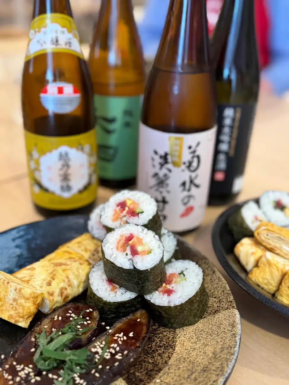 homemade sushi rolls, tamagoyaki, and glazed eggplant served alongside bottles of Japanese sake during a Tokyo washoku (Japanese cuisine) cooking class.