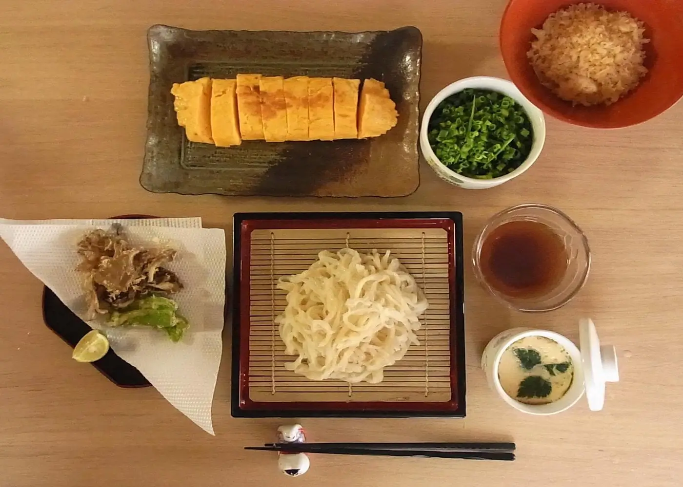 A traditional Japanese meal featuring freshly made udon noodles served on a bamboo tray with dipping sauce, tamagoyaki, tempura vegetables, chopped scallions, grated daikon, and chawanmushi, prepared during a noodle-making class in Tokyo.