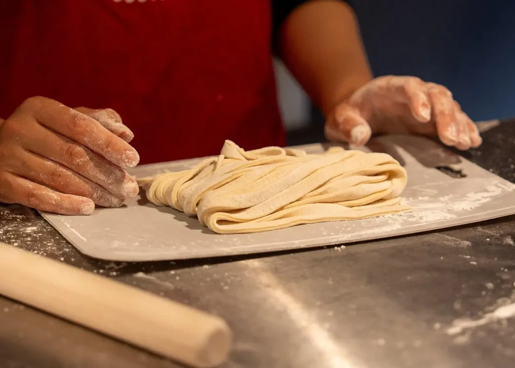 Freshly cut udon noodles on a floured board, with hands covered in dough during a hands-on udon and tempura cooking class in Kyoto.