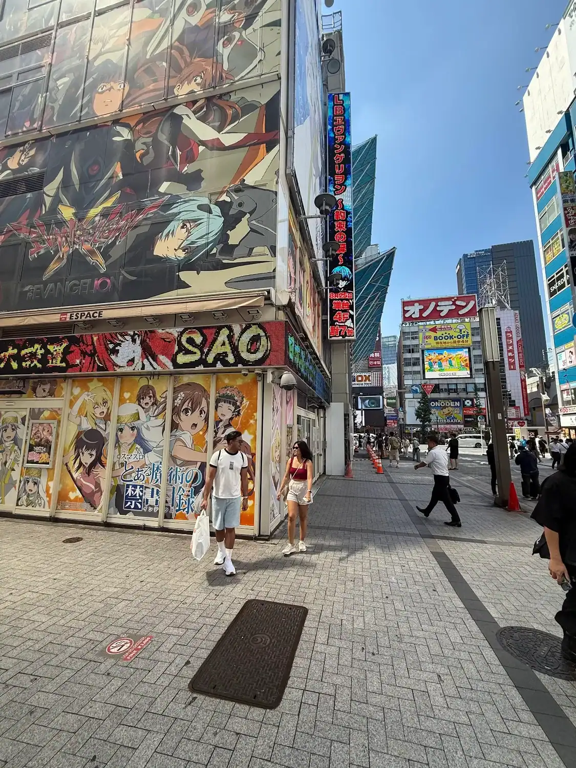 People walking past an anime covered building in Akihabara with bright signs and shops around them.