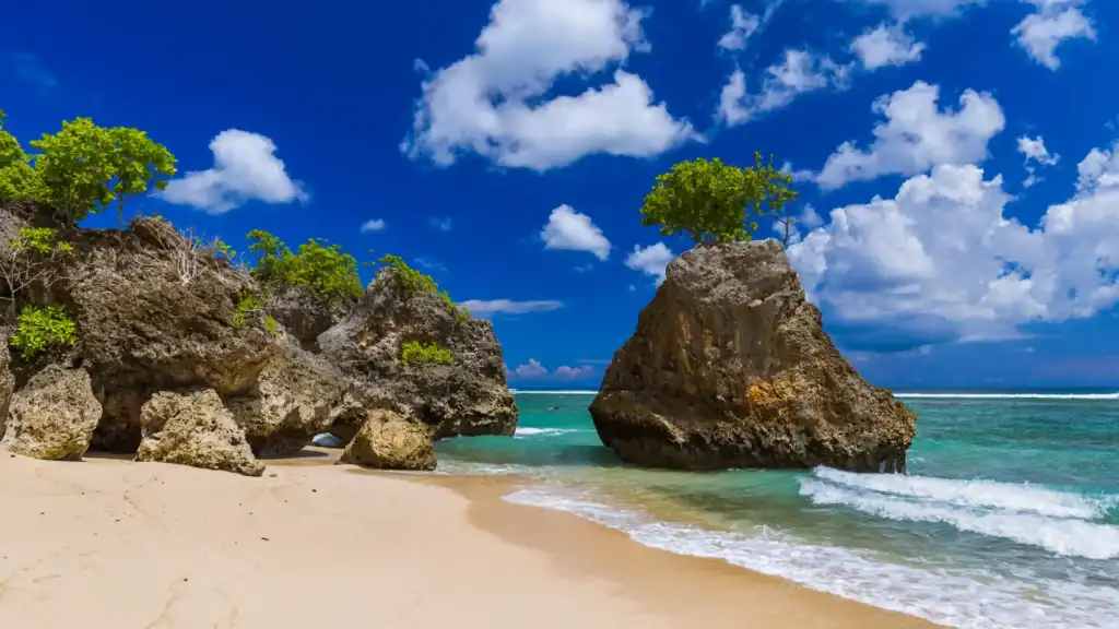 Bingin Beach with large coral rocks, clear blue sea, and bright sky.