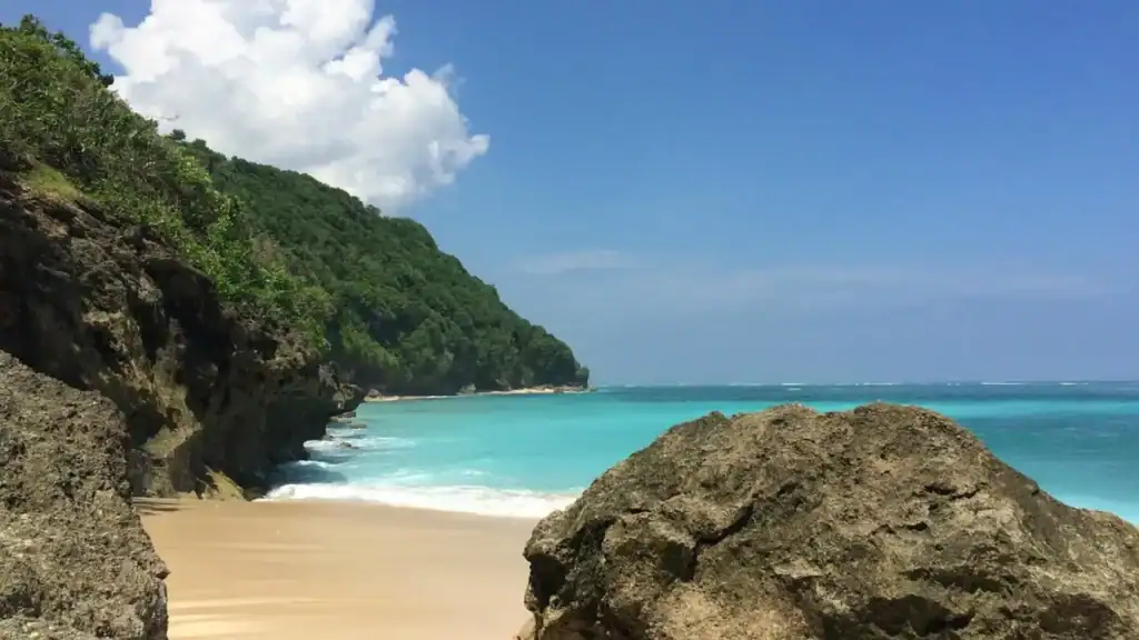 Secluded Green Bowl Beach surrounded by cliffs with bright blue water and golden sand.