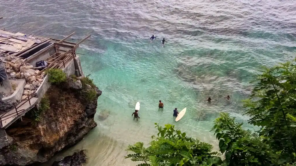 Surfers paddling out through the clear blue water at Suluban. One of the best beaches in Uluwatu