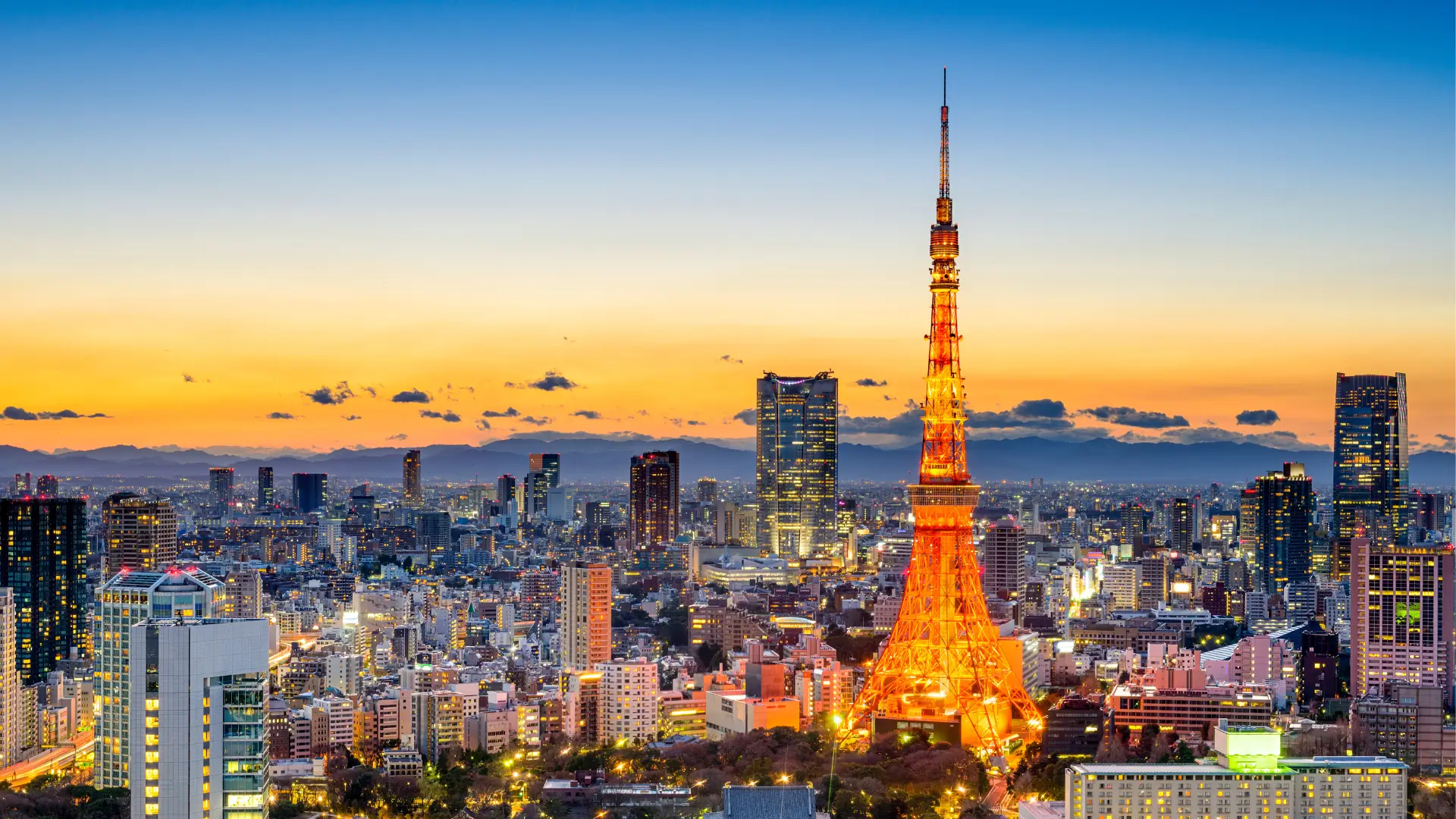 Tokyo skyline at sunset with Tokyo Tower glowing orange above the city buildings.