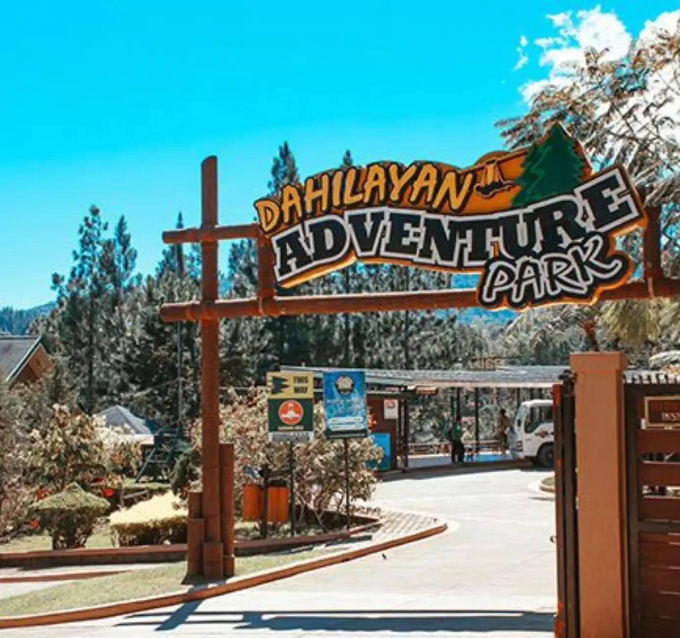 A close-up of the colorful and wavy sign reads "Dahilayan Adventure Park" as it hangs over the road leading to its entrance.