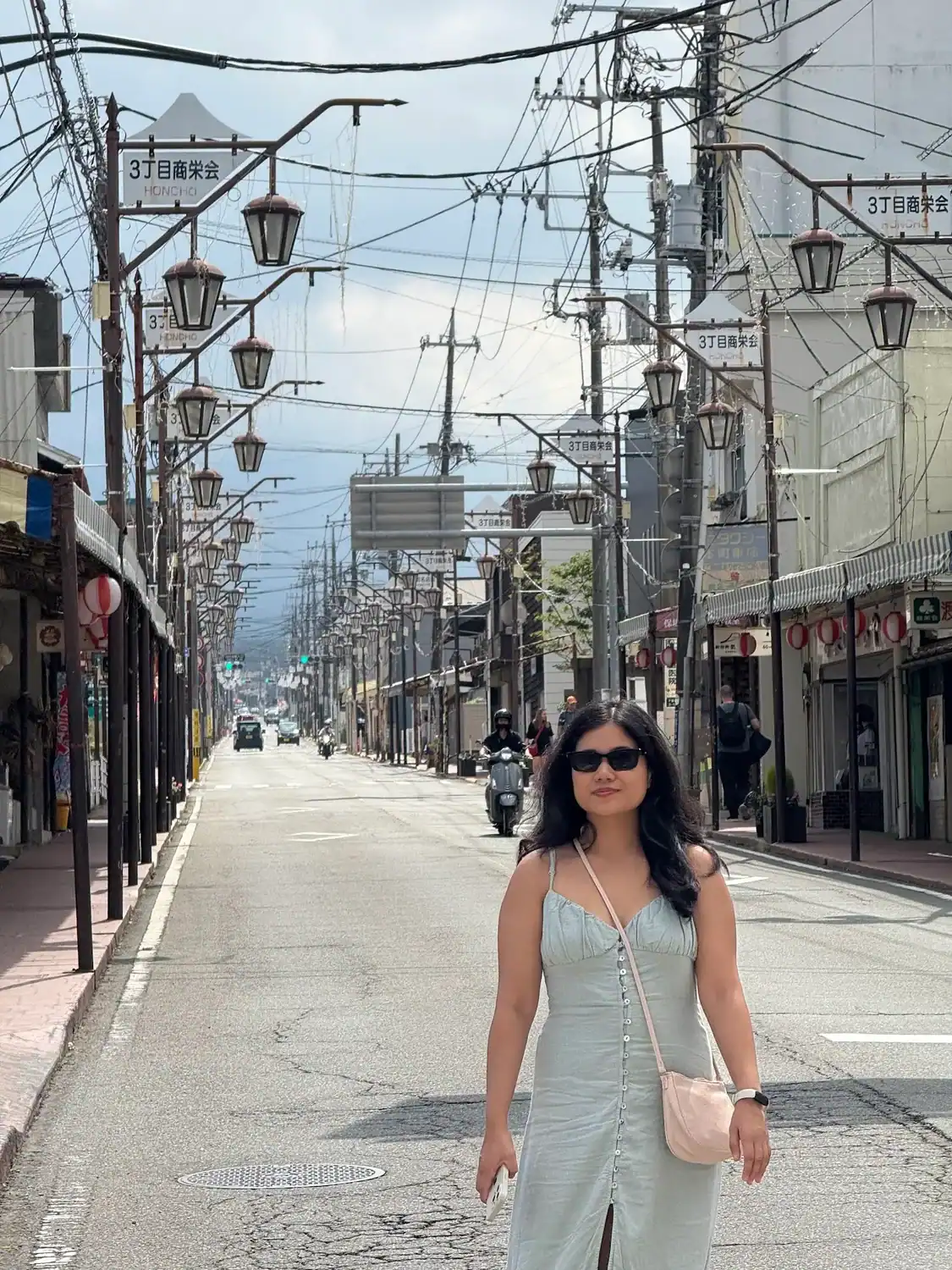 Traveler standing on Honcho Street in Fujiyoshida with Mount Fuji faintly visible in the background on a cloudy day.