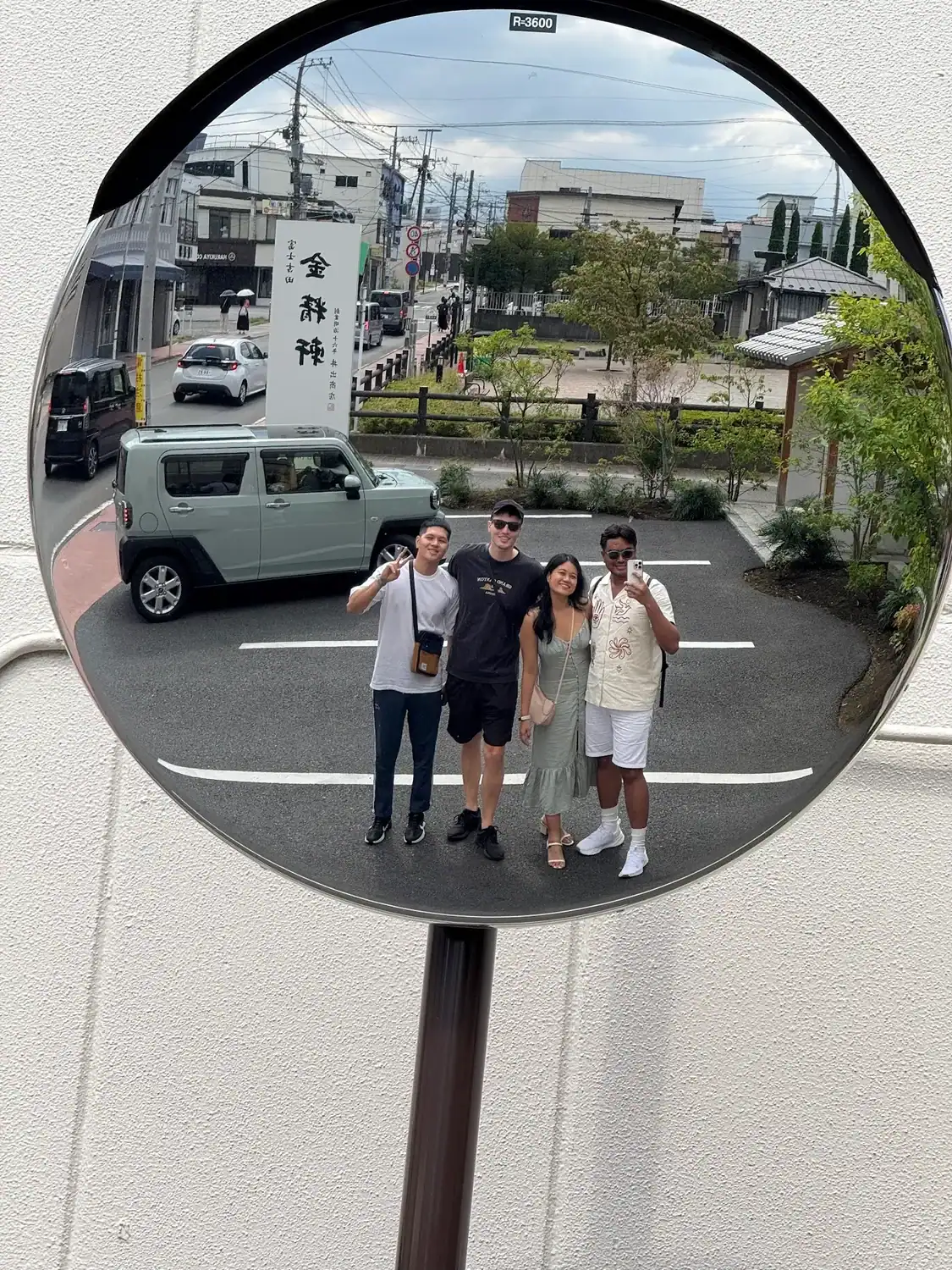 Four friends taking a mirror photo on a street in Japan, with buildings, cars, and a sign in the background.