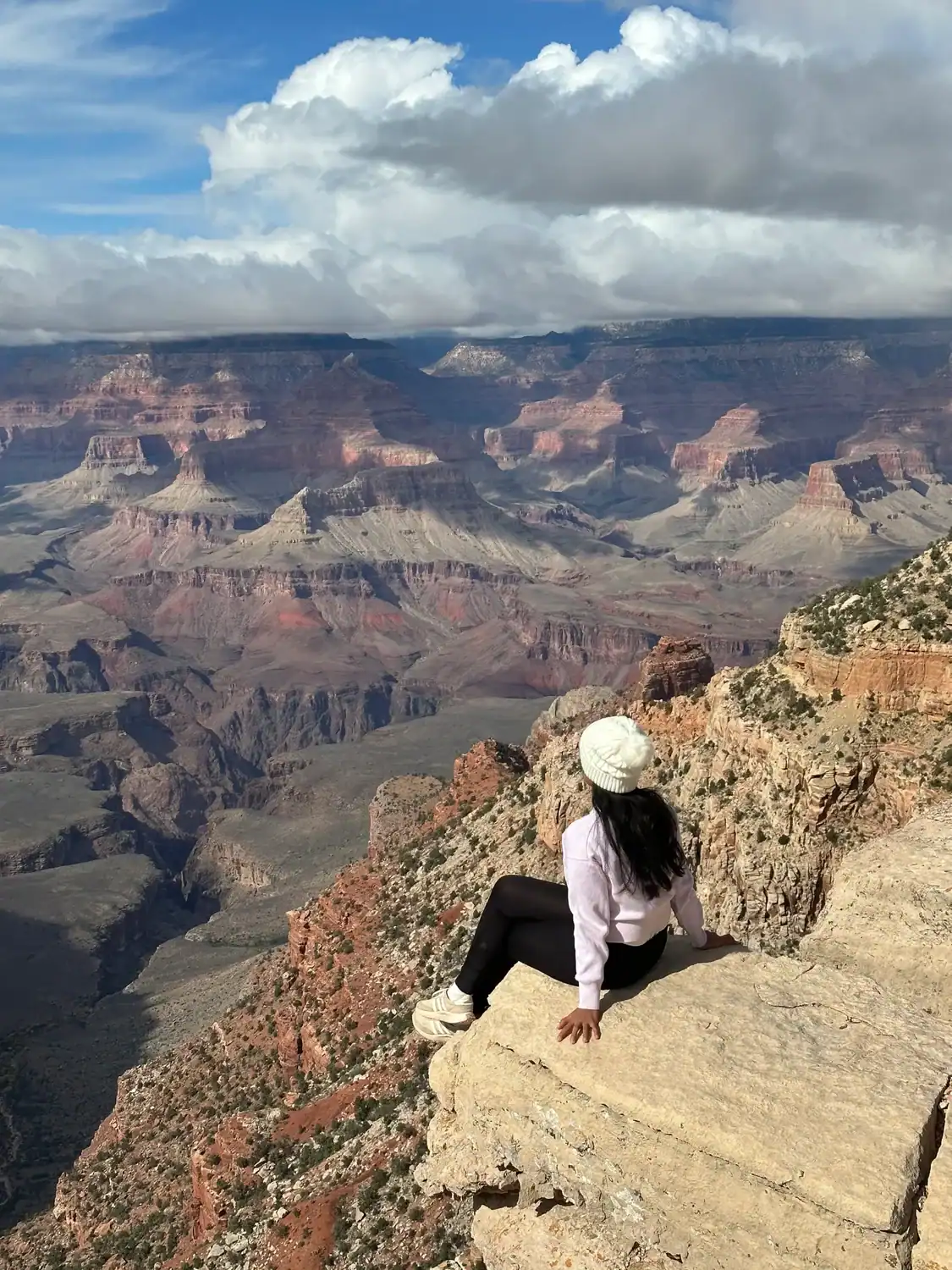 While comparing Worlpackers vs Workaway in terms of workload, an image was shown, featuring a woman sitting on the edge of rocky cliff and overlooking a valley on a clear day.