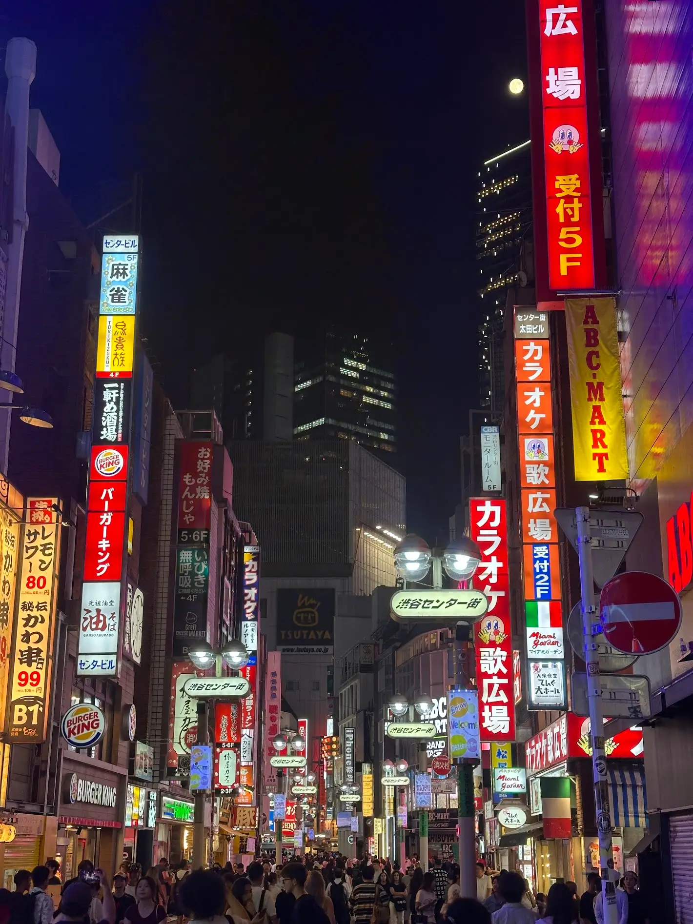 A crowded Tokyo street at night filled with bright neon signs, busy shops, and people walking under the city lights. 2 Day Tokyo Itinerary 