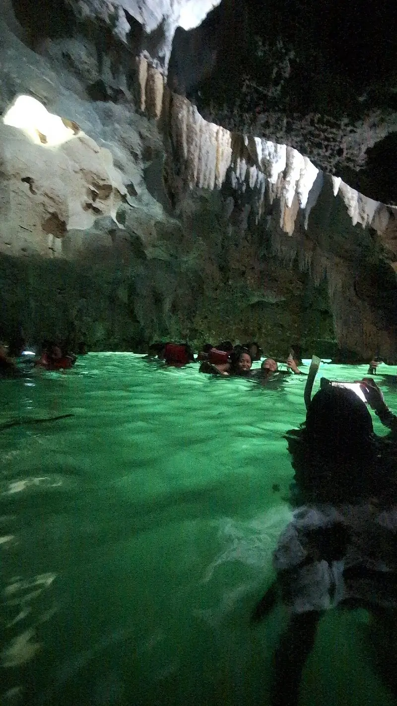 Divers and tourists are submerged in the blue-green waters of Sohoton Cove while rock formations hang over them.