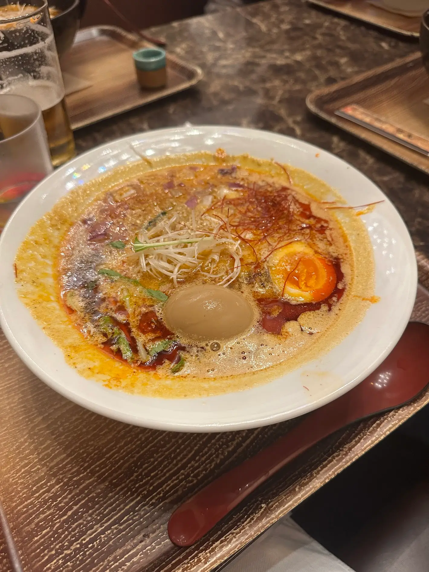 A bowl of spicy ramen with broth, noodles, sliced egg, and chili oil on a wooden table.