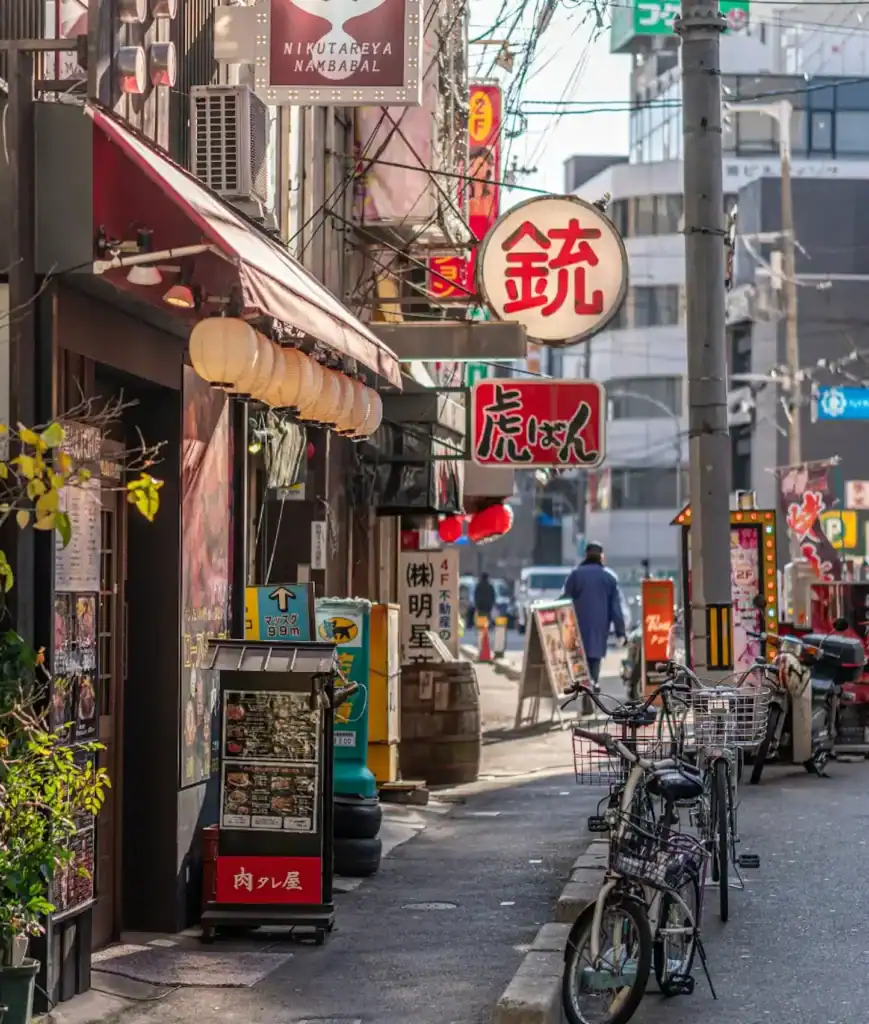 Things to do in Osaka street scene showing a narrow Osaka alley with local restaurants, hanging lanterns, Japanese signs, and parked bicycles during a walking tour.